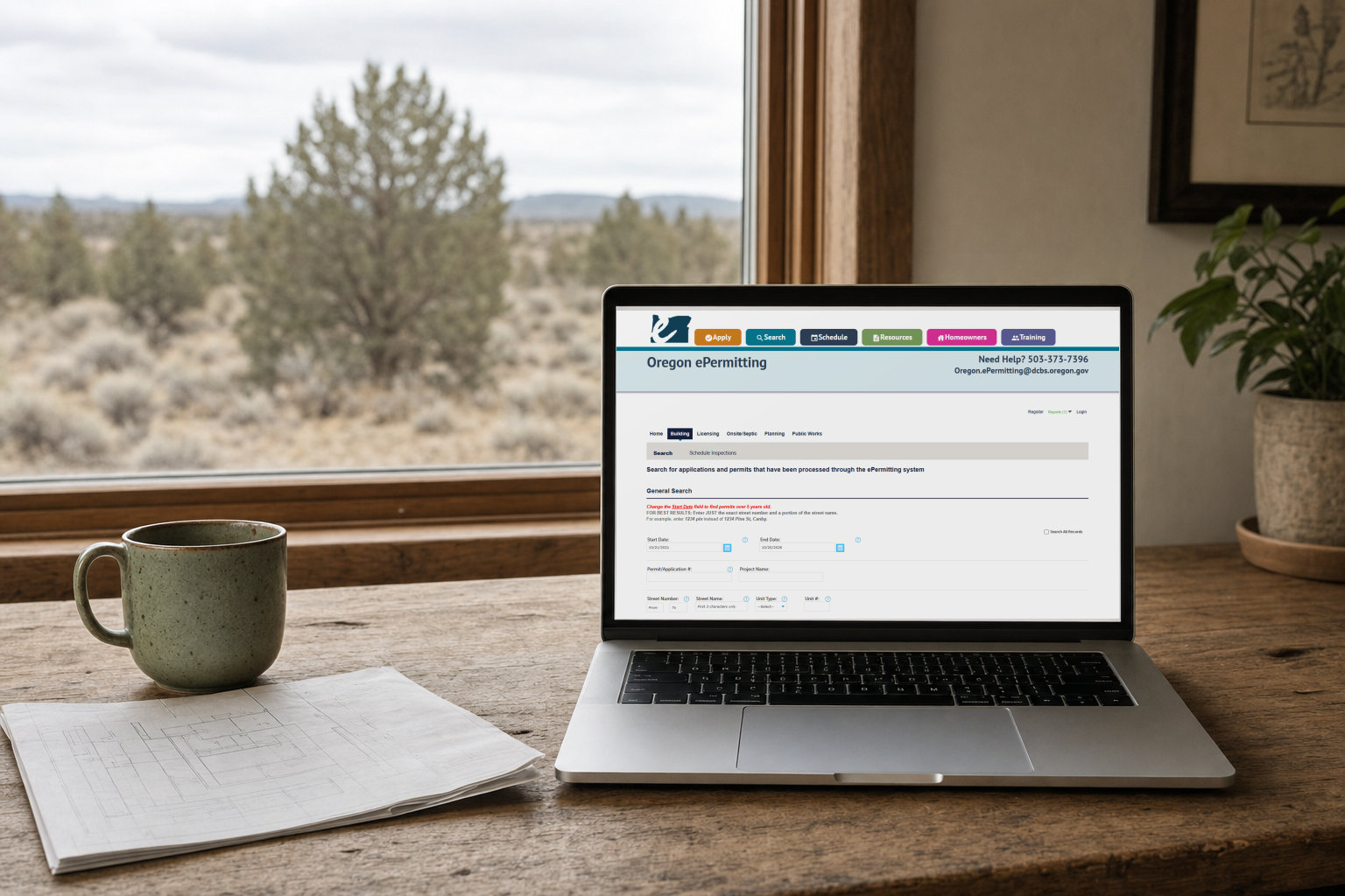 A laptop on a wooden table by a window showing the Oregon ePermitting building permit search page