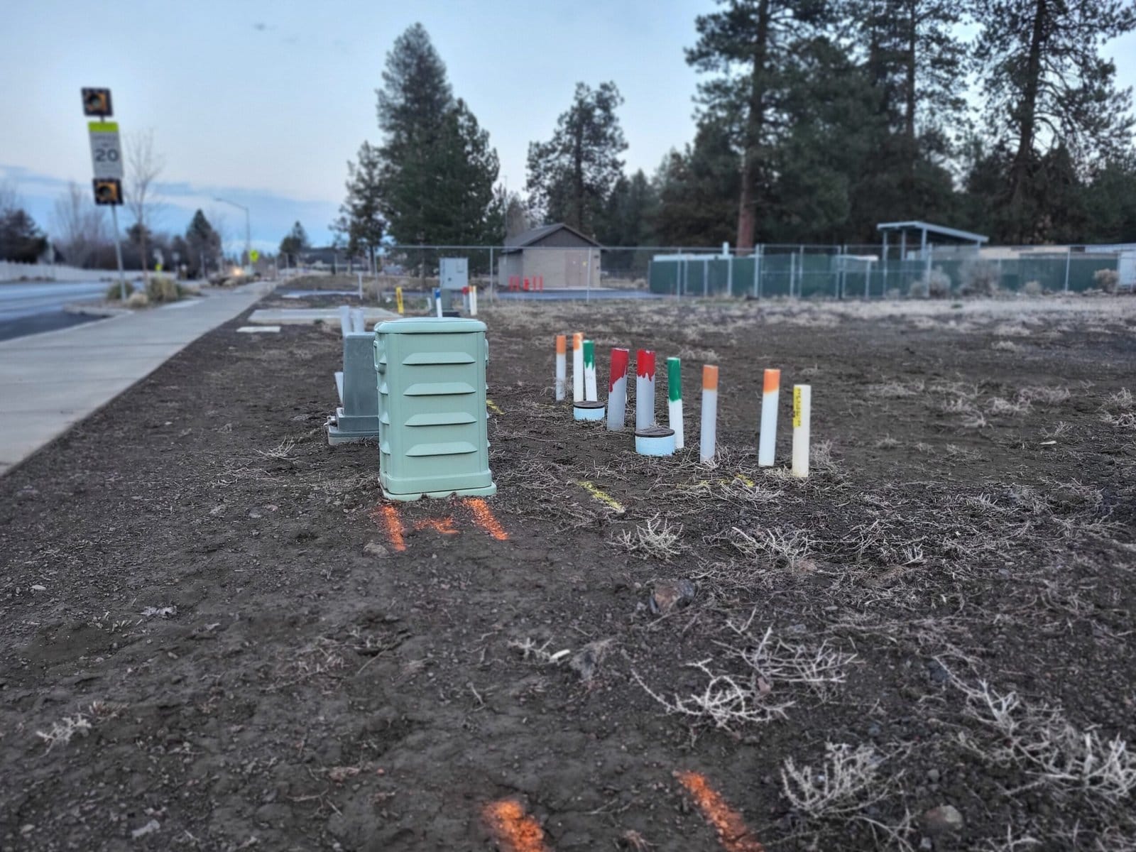 Utility markings and painted stakes on a vacant lot showing locations of underground power, sewer, and gas lines.