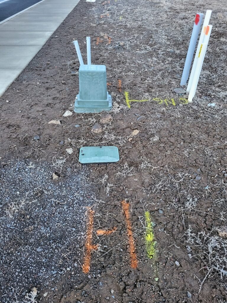 20250327_192634 Utility markings and painted stakes on a vacant lot showing locations of underground power, sewer, and gas lines.
